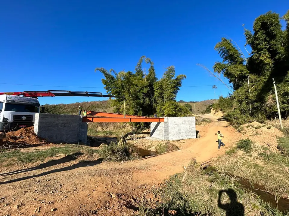 Ponte em construção em Aracitaba, com apoios de concreto e vigas metálicas sendo posicionadas por caminhão guindaste
